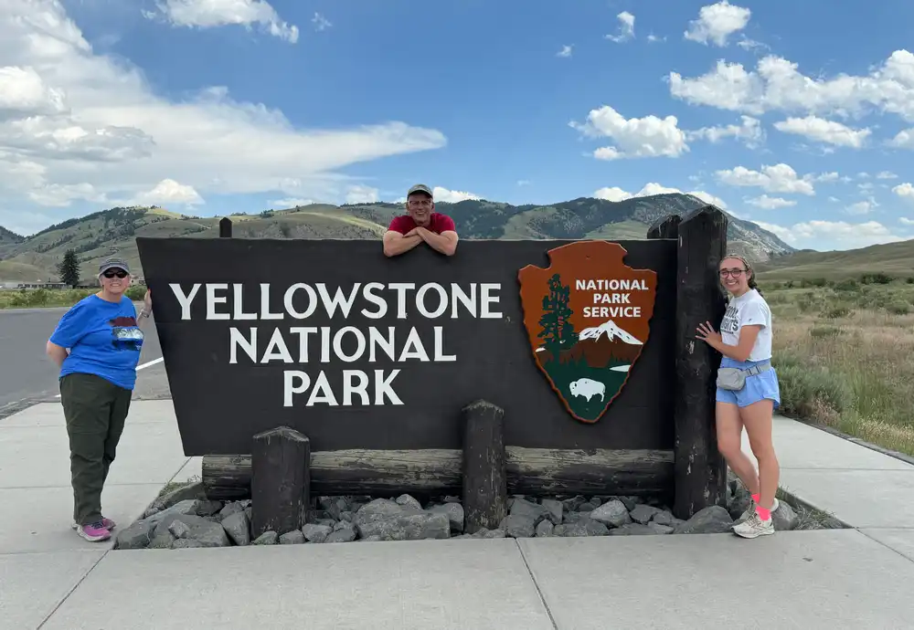Madeline Emerson, Dr. Ropski and Mrs. Ropski around the Yellowstone National Park sign.