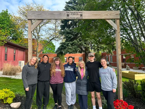 Five ����ֱ�� nursing students and two faculty members stand infront of garden beds they created to support youth mental health initiatives at Harborcreek Youth Services in Erie