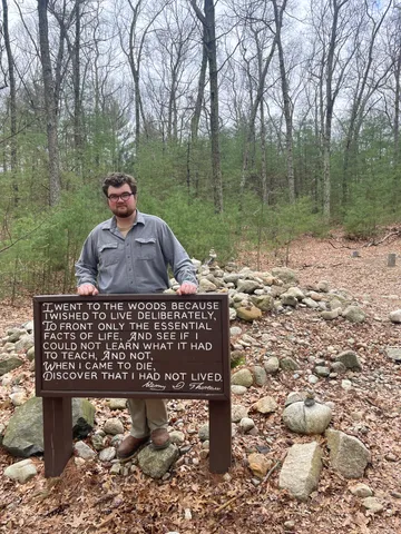 Bratton stands behind a trail sign with a quote from Henry David Thoreau while at his home in Concord, Massachusetts.