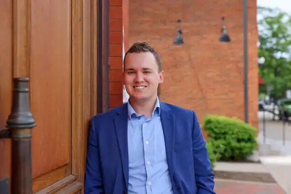 Ethan Bennett smiles at the camera. leaning casually against a wall in downtown Erie