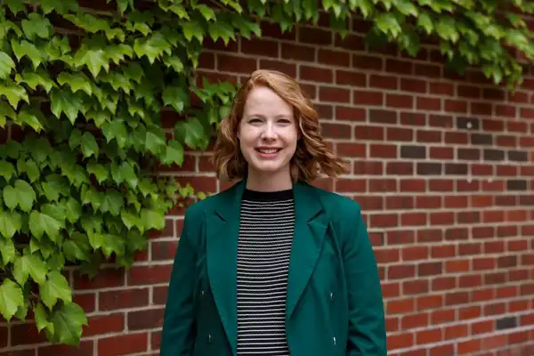 Rachel smiles at the camera in front of a brick wall.