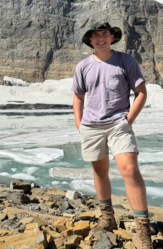 Cooper Cernuska stands in front of a river and wearing a hat and smiling