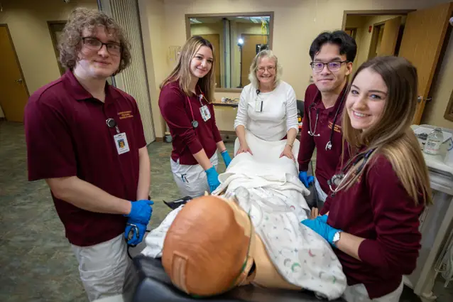4 students standing around a patient simulator, while their professor is giving them instruction