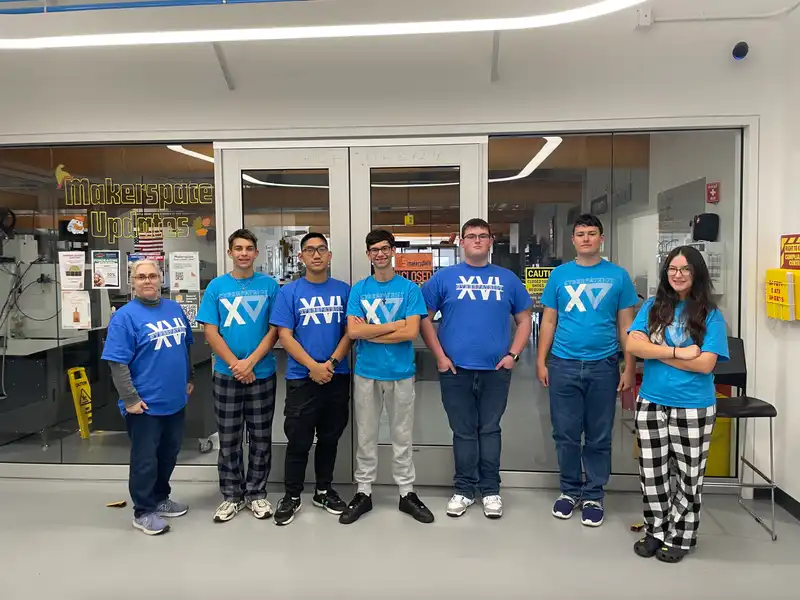 A group of six students and an advisor stand in matching blue shirts, smiling.
