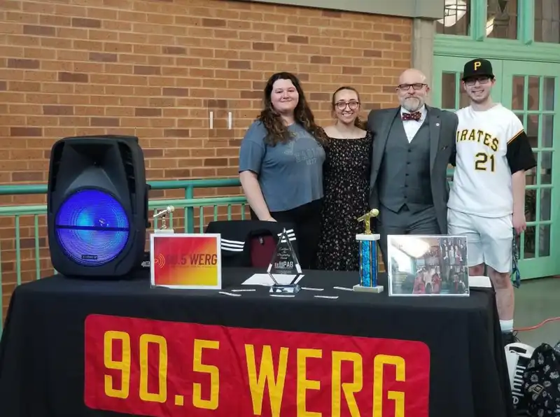 Student DJs from 91's radio station, 90.5 WERG, stand with Dr. Iwanenko behind a table with equipment on it smiling.