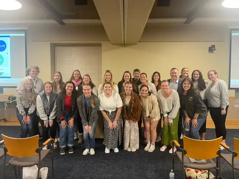 A group of students smile and stand with a speaker at the School of Education's Professional Development Event