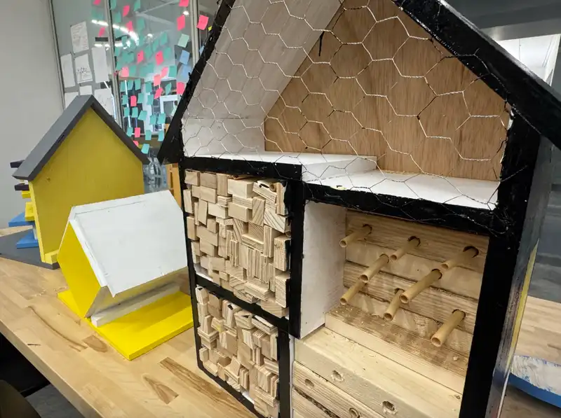 A photo of a bee habitat built in the shape of a house and containing various ephemera to create a comfortable environment for the bee habitat.