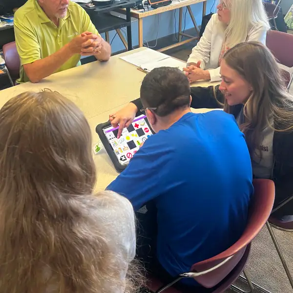 Two student clinicians in ������Ƶ's on-site SLP clinic help a client navigate his AAC device