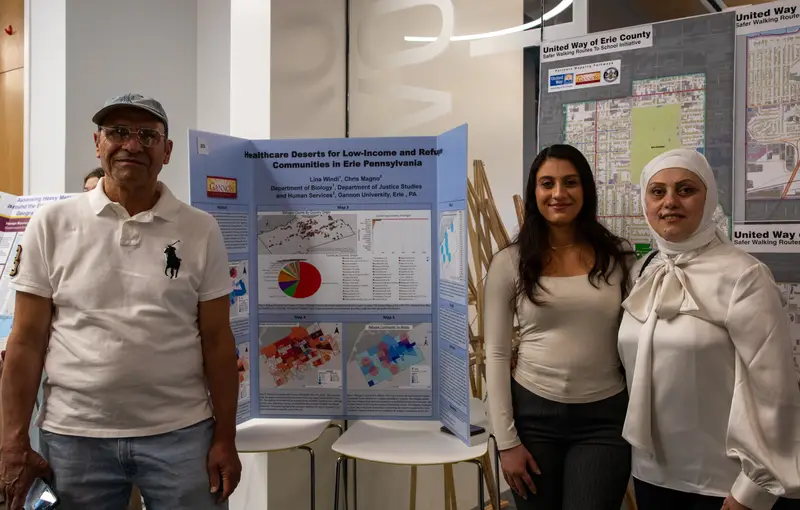 A student stands in front of her GIS poster presentation with her parents