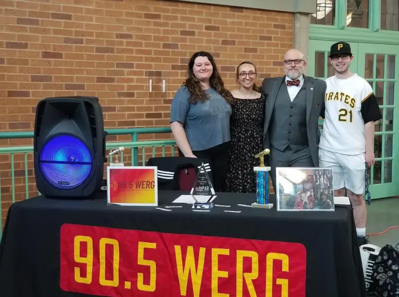 Student DJs from Ƶ's radio station, 90.5 WERG, stand with Dr. Iwanenko behind a table with equipment on it smiling.