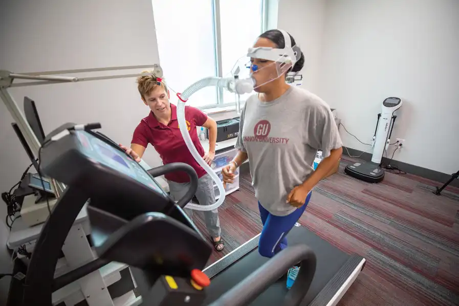 Instructor with student wearing a breathing apparatus while running on a treadmill