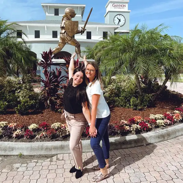 Two students smiling in front of the Golden Knight at the Ruskin Florida Campus